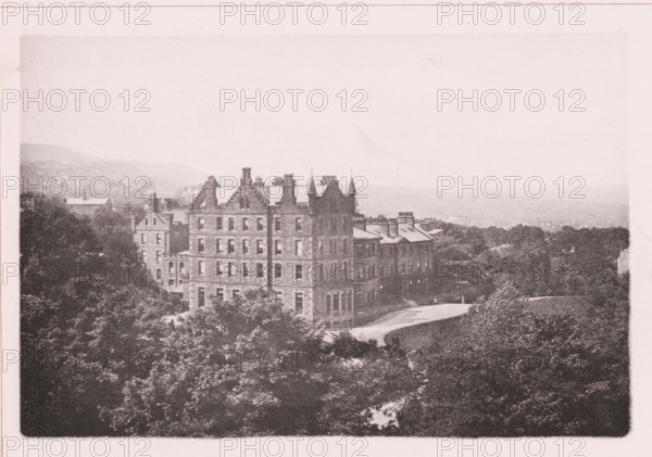 Craigslands hydropathic, page, photomechanical print, c. 1890 - c. 1900, paper, collotype, photoprint, height 101 mm x width 153 mm, medical examination, medical treatment, watering-place, spa, facade (of house or building), A sepia-toned photograph showing a large stone building with multiple stories, steeply pitched roofs, chimneys, and decorative gables, flanked by trees and shrubbery in the foreground and a curved driveway leading past the building, with additional smaller buildings extending to the right and a distant hazy landscape of hills and treetops in the background.