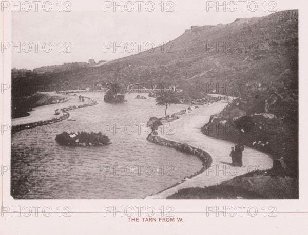 The Tarn from W., page, photomechanical print, c. 1890 - c. 1900, paper, collotype, photoprint, height 101 mm x width 153 mm, lake, mountains, A grainy black-and-white photograph shows a winding waterway bordered by narrow curved paths of light-colored material and low rock edges, with small rocky islets and a few scattered trees rising from the water; several small groups of people in dark clothing stand or walk along the paths, and low hills covered in vegetation rise steeply in the background creating a rugged slope above the scene.