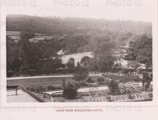 View from Middleton hotel, page, photomechanical print, c. 1890 - c. 1900, paper, collotype, photoprint, height 101 mm x width 153 mm, bridge, A grainy sepia photograph showing a landscape with a stone arched bridge partially obscured by trees, a sloping foreground with planted beds and a bench, expanses of trees and wooded hills in the background, and a small building near the bridge.