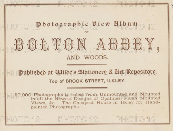Photographic view album of Bolton Abbey and woods, book, inscription: 'ex libris SFJ', publisher: Wild's Stationery and Fine Art Repository, Ilkley, c. 1900, Wild's Stationery and Fine Art Repository, Yorkshire, textile materials, pasteboard, paper, linen (material), printing, collotype, height 157 mm x width 201 mm x thickness 4 mm, A rectangular off-white page with a thin double-lined border and ornate dark brown decorative lettering across the top and center, ornamental flourishes within the larger centered letters, several horizontal rule lines separating sections, a block of smaller dark brown serif text in the lower half arranged in lines, and small scattered brown age spots across the paper.