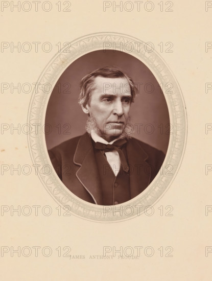 James Anthony Froude, page, photomechanical print, photographer: Lock & Whitfield, cliché maker: anonymous, c. 1871 - in or before 1876, paper, Woodburytype, height 115 mm x width 89 mm, Person, writer, poet, author, historical persons (portraits and scenes from the life) ((full) bust portrait), A sepia-toned oval portrait of an older man with sideburns and short swept hair set against a plain background, mounted on a light cardstock with a decorative oval border around the portrait; the man wears a dark suit jacket with contrasting piping, a waistcoat, a white shirt, and a bow tie, and his expression is neutral as he looks slightly to the side.