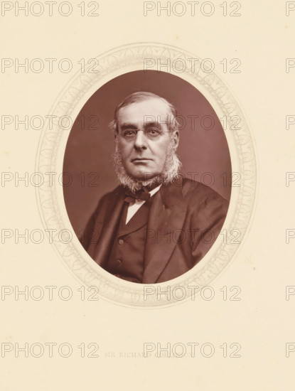 Sir Richard Collinson, page, photomechanical print, photographer: Lock & Whitfield, cliché maker: anonymous, c. 1871 - in or before 1876, paper, Woodburytype, Woodbury Process, height 115 mm x width 89 mm, Person, Richard Collinson, officer, historical persons (portraits and scenes from the life) ((full) bust portrait), An oval sepia portrait of a middle-aged man with sideburns and round spectacles set within an ornate oval mat against a light paper background, the man wearing a dark suit, waistcoat, and bow tie, facing forward with a neutral expression.