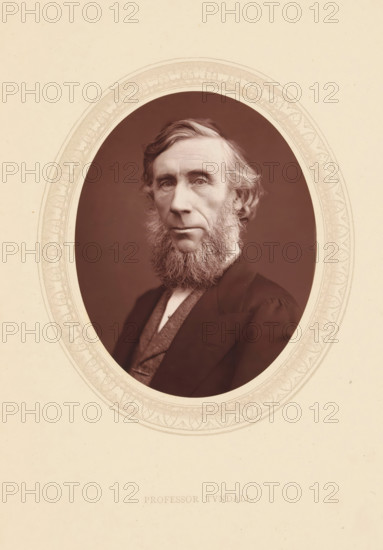 Professor Tyndall, page, photomechanical print, photographer: Lock & Whitfield, cliché maker: anonymous, c. 1871 - in or before 1876, paper, Woodburytype, Woodbury Process, height 115 mm x width 89 mm, Person, John Tyndall, professor, historical persons (portraits and scenes from the life) ((full) bust portrait), An oval photographic portrait of an older man with a full beard and sideburns set against a dark background, framed by a decorative pale oval border on a light textured background, showing the man's face turned slightly toward the viewer with wavy hair, a high forehead, deep-set eyes, a prominent nose, and a closed mouth; he wears a dark jacket over a lighter vest and high-collared shirt, and the overall image has a sepia tone.