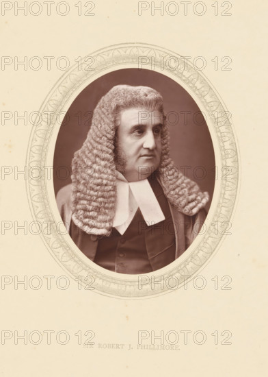 Sir Robert J. Phillimore, page, photomechanical print, photographer: Lock & Whitfield, cliché maker: anonymous, c. 1871 - in or before 1876, paper, Woodburytype, Woodbury Process, height 115 mm x width 89 mm, Person, Robert Phillimore, magistracy, judges, historical persons (portraits and scenes from the life) ((full) bust portrait), A sepia-toned portrait of a man shown from the chest upward inside an ornate oval frame, wearing a full curled judicial wig with tight rows of ringlets falling to his shoulders, a dark formal coat and a white collar with two flat tabs, the man looking slightly to his left with a neutral expression and visible sideburns, the oval frame set against a pale background with subtle speckling.