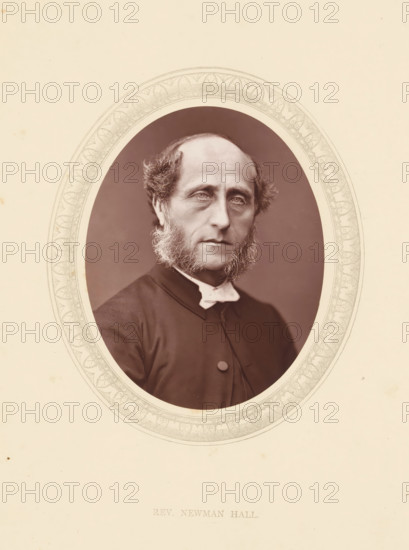 Rev. Newman Hall, page, photomechanical print, photographer: Lock & Whitfield, cliché maker: anonymous, c. 1871 - in or before 1876, paper, Woodburytype, Woodbury Process, height 115 mm x width 89 mm, Person, Christopher Newman Hall, historical persons (portraits and scenes from the life) ((full) bust portrait), A sepia-toned oval portrait of a middle-aged man with a high forehead and receding hairline, framed by sideburns that extend down into a full beard along his jaw, wearing a dark clerical coat with a visible button and a white clerical collar, set against a plain darker background and surrounded by a decorative oval mat with an intricate patterned border, all on a light cream paper with small spots and slight discoloration.