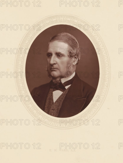 EM Ward, RA, page, photomechanical print, photographer: Lock & Whitfield, cliché maker: anonymous, c. 1873 - in or before 1878, paper, Woodburytype, Woodbury Process, height 115 mm x width 89 mm, Person, Edward Matthew Ward, portrait, self-portrait of painter, historical persons (portraits and scenes from the life) ((full) bust portrait), A sepia oval portrait of a middle-aged man with neatly combed hair and prominent sideburns, shown from the chest up and wearing a dark jacket, a patterned waistcoat, a white shirt, and a tied bow at the collar, set against a dark background and surrounded by a decorative oval border on a light-colored mount.