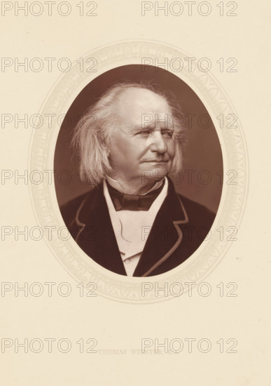 Thomas Webster, RA, page, photomechanical print, photographer: Lock & Whitfield, cliché maker: anonymous, c. 1873 - in or before 1878, paper, Woodburytype, Woodbury Process, height 115 mm x width 89 mm, Person, portrait, self-portrait of painter, historical persons (portraits and scenes from the life) ((full) bust portrait), An oval sepia-toned portrait of an older man with shoulder-length light hair swept back, visible facial wrinkles, and a composed expression, shown from the chest up wearing a dark jacket with a light-colored shirt and a bow tie, set against a dark oval background and framed by a decorative light-colored oval border on a light page.