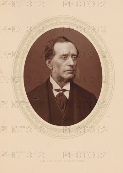 Sir Leopold McClintock, page, photomechanical print, photographer: Lock & Whitfield, cliché maker: anonymous, c. 1873 - in or before 1878, paper, Woodburytype, Woodbury Process, height 115 mm x width 89 mm, Person, Francis Leopold McClintock (sir), explorer, historical persons (portraits and scenes from the life) ((full) bust portrait), An oval-framed sepia portrait of a middle-aged man shown from the chest up, wearing a dark suit, waistcoat, high-collared shirt, and a cravat; he has short, neatly combed hair, prominent sideburns, and a composed facial expression while looking slightly to his right; the oval image is surrounded by a decorative patterned border set against a plain light background.
