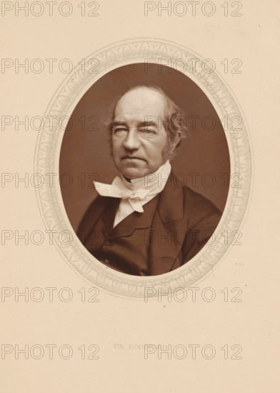 Dr. Goodford, page, photomechanical print, photographer: Lock & Whitfield, cliché maker: anonymous, c. 1873 - in or before 1878, paper, Woodburytype, Woodbury Process, height 115 mm x width 89 mm, Person, Charles Old Goodford, historical persons (portraits and scenes from the life) ((full) bust portrait), A sepia portrait of an older man shown from the chest up within an ornate oval frame, wearing a dark suit jacket and a white neckcloth tied in a bow, with short wavy hair and prominent sideburns, a furrowed forehead, and a neutral expression, set against a plain light background.
