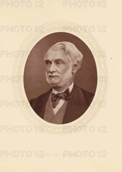Lord John Manners, page, photomechanical print, photographer: Lock & Whitfield, cliché maker: anonymous, c. 1873 - in or before 1878, paper, Woodburytype, Woodbury Process, height 115 mm x width 89 mm, Person, John Manners (1818-1906), politician, eg party leader, historical persons (portraits and scenes from the life) ((full) bust portrait), An oval sepia portrait of an older man with light hair and sideburns set against a dark background, framed by a decorative oval border on a light beige page; he is shown from the chest up wearing a dark jacket, a waistcoat with a patterned texture, a white shirt, and a tied bow at the collar, his gaze directed slightly to one side and his expression neutral.