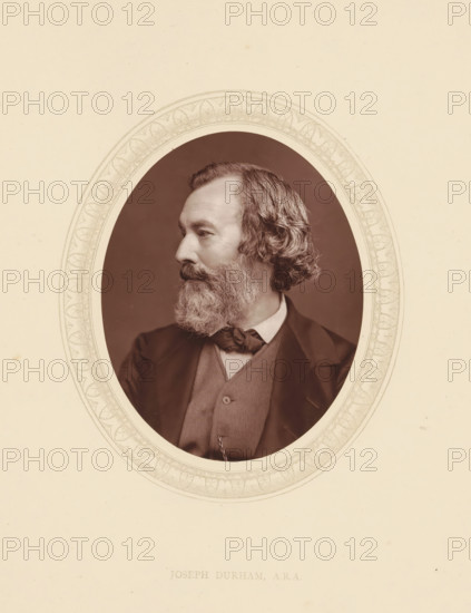 Joseph Durham, ARA, page, photomechanical print, photographer: Lock & Whitfield, cliché maker: anonymous, c. 1873 - in or before 1877-10-27, paper, Woodburytype, Woodbury Process, height 115 mm x width 89 mm, Person, Joseph Dunham, portrait, self-portrait of sculptor, historical persons (portraits and scenes from the life) ((full) bust portrait), A sepia oval portrait of a man shown in profile facing left, with wavy hair and a full beard, wearing a suit jacket, waistcoat, high-collared shirt, and bow tied at the neck, set against a plain dark background and framed by a decorative oval border on a light background.