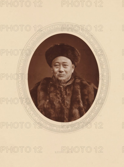 Kuo Tajen, page, photomechanical print, photographer: Lock & Whitfield, cliché maker: anonymous, c. 1875 - in or before 1880, paper, Woodburytype, Woodbury Process, height 115 mm x width 89 mm, Person, Guo Songtao, diplomacy, diplomat, historical persons (portraits and scenes from the life) ((full) bust portrait), A sepia-toned oval portrait centered on a pale background shows an older man wearing a dark fur hat and a heavy fur coat, his face with a mustache and a goatee, with a calm expression and slightly upturned eyes; the oval is framed by an ornate decorative border with repeating leaf-like and scroll motifs.