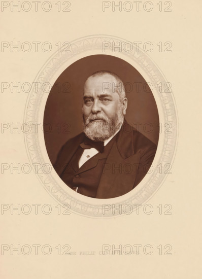 Sir Philip Cunliffe Owen, page, photomechanical print, photographer: Lock & Whitfield, cliché maker: anonymous, c. 1875 - in or before 1880, paper, Woodburytype, Woodbury Process, height 115 mm x width 89 mm, Person, Philip Cunliffe-Owen, director, boss (in modern industry), historical persons (portraits and scenes from the life) ((full) bust portrait), An oval portrait of an older man with a full beard and short hair set against a dark background, framed by a decorative oval border on a light-colored page, the man wearing a dark suit jacket with a vest and a bow tie, his gaze directed slightly forward and his expression neutral.