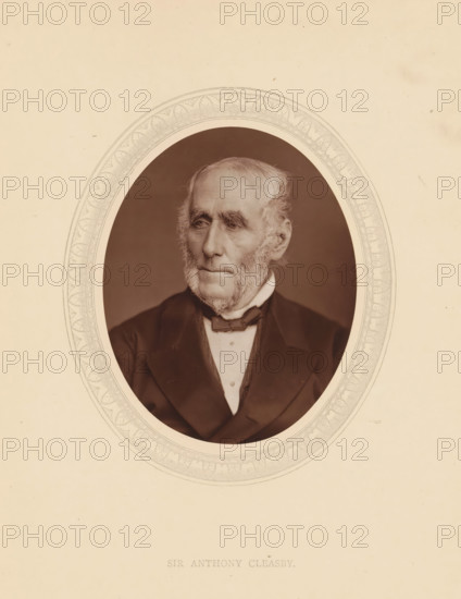 Sir Anthony Cleasby, page, photomechanical print, photographer: Lock & Whitfield, cliché maker: anonymous, c. 1875 - in or before 1880, paper, Woodburytype, Woodbury Process, height 115 mm x width 89 mm, Person, Anthony Claesby, magistracy, judges, historical persons (portraits and scenes from the life) ((full) bust portrait), An oval-framed sepia portrait of an elderly man with light hair and prominent sideburns, wearing a dark suit jacket, a white shirt, and a bow tie, set against a plain background; the oval frame has a decorative patterned border and the portrait is centered on a light-colored sheet with some small blemishes and spots.