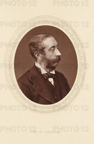 Earl of Carnarvon, page, photomechanical print, photographer: Lock & Whitfield, cliché maker: anonymous, c. 1875 - in or before 1880, paper, Woodburytype, Woodbury Process, height 115 mm x width 89 mm, Person, Henry Herbert, politician, eg party leader, historical persons (portraits and scenes from the life) ((full) bust portrait), A sepia oval portrait of a man in three-quarter profile facing right, framed by a decorative patterned border set on a light background, showing the man's wavy short hair, prominent mustache and sideburns, high forehead, and contemplative expression; he wears a dark jacket with a visible lapel, a white shirt collar, a bow tied at the neck, and a waistcoat beneath, all photographed against a plain dark backdrop within the ornate oval frame.