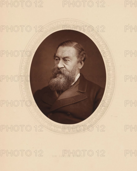 Sir Samuel Baker, page, photomechanical print, photographer: Lock & Whitfield, cliché maker: anonymous, c. 1875 - in or before 1880, paper, Woodburytype, Woodbury Process, height 115 mm x width 89 mm, Person, Samuel White Baker, explorer, historical persons (portraits and scenes from the life) ((full) bust portrait), A sepia-toned oval portrait of an older man with a full bushy beard and mustache, neatly combed hair, and a solemn expression, dressed in a dark formal coat with visible lapels, set against a plain dark background and surrounded by a decorative oval border on a light beige mount.