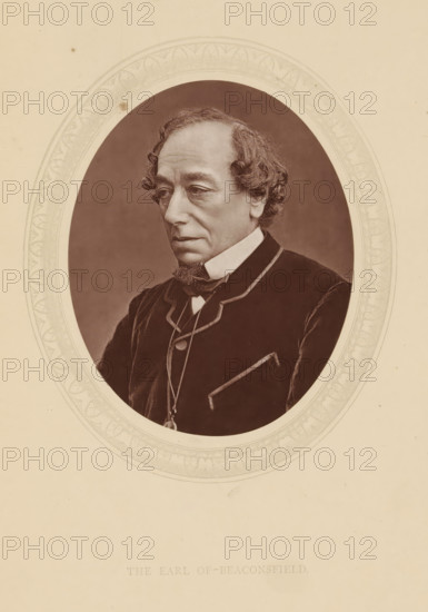 The earl of Beaconsfield, page, photomechanical print, photographer: Downey, William & Daniel, cliché maker: anonymous, c. 1876 - in or before 1881, paper, Woodburytype, Woodbury Process, height 115 mm x width 89 mm, Person, Benjamin Disraeli, politician, eg party leader, historical persons (portraits and scenes from the life) ((full) bust portrait), A sepia-toned oval portrait of an older man with wavy hair and sideburns, shown from the chest up and turned slightly to his left, wearing a dark coat with light piping, a high white collar, a bow tie, and a pendant on a chain; the portrait is set within a decorative oval frame on a pale background.