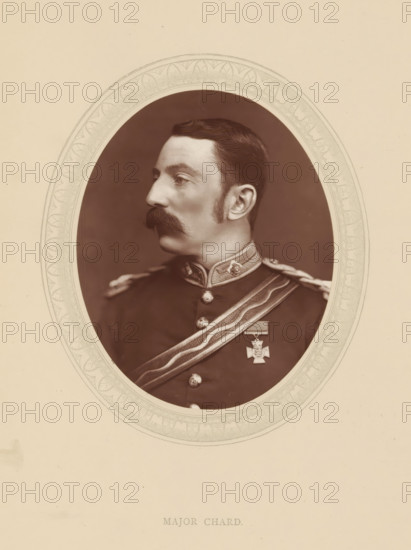 Major Chard, page, photomechanical print, photographer: Lock & Whitfield, cliché maker: anonymous, c. 1876 - in or before 1881, paper, Woodburytype, Woodbury Process, height 115 mm x width 89 mm, Person, John Chard, officer, historical persons (portraits and scenes from the life) ((full) bust portrait), A sepia oval portrait of a man in a military uniform shown in profile facing left, with dark hair combed back and a thick mustache, wearing a high-collared jacket with decorative trim and metal buttons, a sash across his chest with braided cords on the shoulder, and a medal pinned to the jacket, all set against a plain darker background and framed by an ornate patterned oval mat on a light-colored page.
