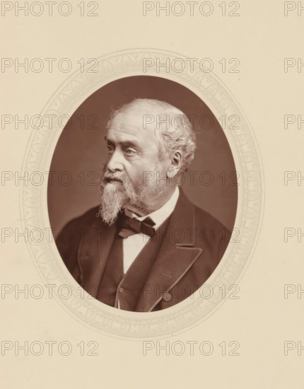 William Harrison Ainsworth, page, photomechanical print, photographer: Lock & Whitfield, cliché maker: anonymous, c. 1876 - in or before 1881, paper, Woodburytype, Woodbury Process, height 115 mm x width 89 mm, Person, portrait of a writer, historical persons (portraits and scenes from the life) ((full) bust portrait), An oval sepia portrait of an older man with a full beard and mustache, his hair receding and curled at the sides, shown in three-quarter profile looking left, wearing a dark suit jacket with wide lapels, a waistcoat, a collared shirt, and a bow tie, set against a plain dark background and framed by an ornate decorative oval border on a light background.