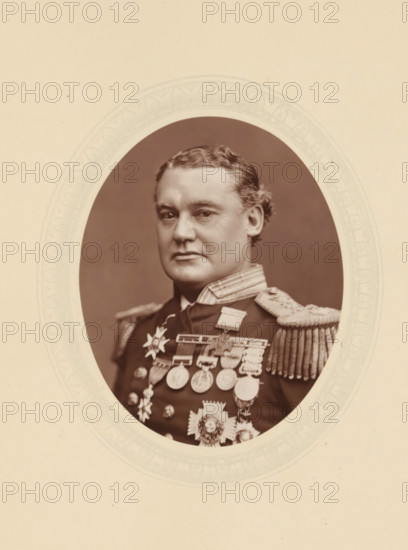 Sir William Hewett, page, photomechanical print, photographer: Lock & Whitfield, cliché maker: anonymous, c. 1877 - in or before 1882, paper, Woodburytype, Woodbury Process, height 115 mm x width 89 mm, Person, William Nathan Wrighte Hewett, officer, historical persons (portraits and scenes from the life) ((full) bust portrait), An oval sepia portrait shows a man from the chest up wearing a dark military uniform with ornate shoulder epaulettes and a high collar; he has wavy hair combed back and a composed facial expression, and his chest is adorned with multiple medals and decorative insignia; the portrait is set against a plain darker background and framed by a patterned oval mat on a light-colored mount.