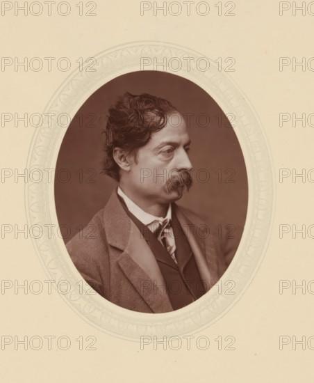 William Quiller Orchardson, page, photomechanical print, photographer: Lock & Whitfield, cliché maker: anonymous, c. 1877 - in or before 1882, paper, Woodburytype, Woodbury Process, height 115 mm x width 89 mm, Person, portrait, self-portrait of painter, historical persons (portraits and scenes from the life) ((full) bust portrait), An oval sepia photograph of a man shown in profile facing right, with wavy dark hair and a full mustache, wearing a collared shirt, tie, waistcoat, and an overcoat, set against a plain dark background and surrounded by a decorative light-colored oval mat with a patterned border on a neutral page.