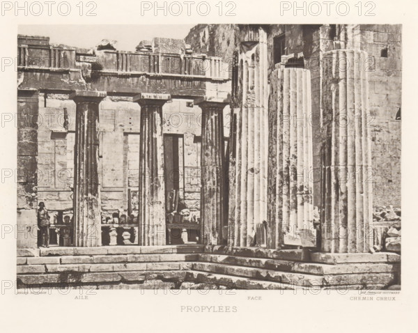 Propylées, Propylées of the Acropolis of Athens, page, photomechanical print, inscription: 'Aile Face Chemin creux', Athens, cliché maker: Dujardin, printer (person): Chardon-Wittmann, c. 1880 - in or before 1890, photographer, printer (person), Athene, Periféreia Protevoúsis, paper, photoaquatint, height 145 mm x width 215 mm, ruin of a building, architecture, column, pillar, gate, entrance, staircase, Acropolis, Propylaea (Athens), A sepia-toned photograph showing a stone entrance with tall fluted columns and a stepped platform in front, weathered block walls and lintels above the columns, a row of balustrades and sculpted fragments visible behind the columns, and a person standing near one of the columns; the stone surfaces display chips, stains, and textured aging.