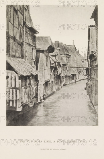 View of the Risle at Pont-Audemer, Une vue de la Risle, a Pont-Audemer (Eure), page, photomechanical print, number: 'Pl. VI.', photographer: G. Robard, Pont-Audemer, c. 1885 - in or before 1895, paper, collotype, photoprint, height 186 mm x width 144 mm, river, façade (of house or building), Risle, A narrow waterway runs between rows of closely packed timber-framed buildings with steep, uneven roofs and projecting upper floors, the façades showing visible beams, plaster, and brickwork, many windows of varying sizes and some overhanging eaves; the surface of the water appears rippled and reflective, and a simple wooden footbridge spans the channel between the buildings further along, while chimneys and rooflines create a jagged skyline against a pale sky.