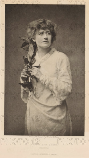 Miss Ellen Terry (Ophelia), page, photomechanical print, photographer: Window & Grove, cliché maker: anonymous, publisher: Virtue & Co., London, c. 1880 - in or before 1890, paper, photoaquatint, height 196 mm x width 121 mm, Person, Ellen Terry, portrait of actor, actress, A portrait of a woman shown from head to mid-thigh wearing a light-colored dress with long sleeves, her hair styled in loose waves, holding a sprig of leaves and small clustered flowers near her chest, looking slightly upward and to the side against a plain dark background with a light border around the image.