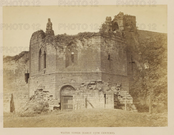 Water Tower (Early 13th Century), Ruin of a water tower of Kenilworth Castle, photograph, page, Kenilworth Castle, c. 1862 - in or before 1872, photographer, Kenilworth, paper, albumen print, height 152 mm x width 204 mm, Photo opposite title page., ruin of a dwelling, house, castle, A weathered stone building with arched windows and openings sits on a grassy slope, its upper walls partly crumbled and overgrown with vines and vegetation, a gated doorway set into the lower wall beneath a bricked arch, rough rubble piled around the base, a taller ruined section with masonry blocks and a narrow vertical slit opening, trees and foliage visible to one side, and a plain sky above.