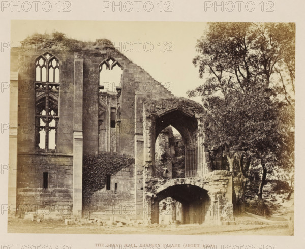 The great Hall, eastern façade (about 1392), View of the ruin of the façade of the hall of Kenilworth Castle, photograph, page, Kenilworth Castle, c. 1862 - in or before 1872, photographer, Kenilworth, paper, albumen print, height 152 mm x width 204 mm, ruin of a dwelling, house, castle, façade (of house or building), A sepia-toned photograph of a ruined stone building showing part of a large facade with tall gothic window openings and pointed arches, weathered masonry with visible blocks and ivy climbing one wall, collapsed sections with rubble and broken stonework, an arched doorway leading into shadowed interior spaces, and a large leafy tree growing beside the ruins.