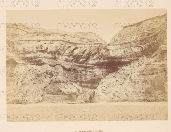 Blackgang Chine, photograph, page, photographer: Frank Mason Good, Isle of Wight, c. 1859 - in or before 1869, paper, albumen print, height 100 mm x width 144 mm, rocky coast, coastal cliff or crag, A sepia-toned photograph of a steep rocky cliff face with layered horizontal strata and eroded textures, showing dark shadowed recesses and lighter weathered surfaces; a narrow stepped path carved into the rock leads up from the lower central area into a small dark opening; the foreground is a flat sandy or pebbled beach area, and the upper portion of the image shows a pale sky above the cliff rim.