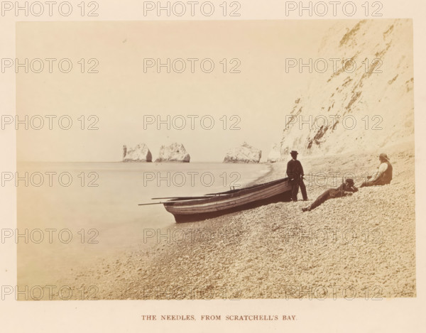 The Needles from Scratchell's Bay, photograph, page, photographer: Frank Mason Good, Scratchell's Bay, c. 1859 - in or before 1869, Frank Mason Good, photographer, Isle of Wight, paper, albumen print, height 100 mm x width 144 mm, rocky coast, coastal cliff or crag, Needles, The, A pebble beach slopes down to calm water with three wooden rowboats pulled up at the shore, one boat positioned nearest the foreground with oars resting across its interior. Three people sit and stand near the boats on the pebbles; one person stands beside the nearest boat wearing a dark jacket and a hat, another reclines on the pebbles with head propped and legs extended, and a third sits facing the water wearing a head covering and vest. Tall white cliffs rise steeply along the right side of the scene with textured rock faces and scattered darker streaks, and several rocky sea stacks emerge from the water a short distance offshore with a slender cylindrical structure on the nearest stack. The overall image h...