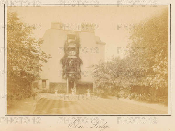 Elm Lodge, photograph, page, photographer: J. Perry, England, c. 1872 - in or before 1882, paper, albumen print, height 103 mm x width 152 mm, garden, housing, façade (of house or building), A faded sepia photograph of a multi-story house with a central entrance and windows, the facade partially covered by climbing foliage around a central vertical section, flanked by trees and shrubs on both sides, a driveway leading up to the entrance with decorative urns positioned near the doorway, chimneys visible at the roofline, and a framed border around the image.