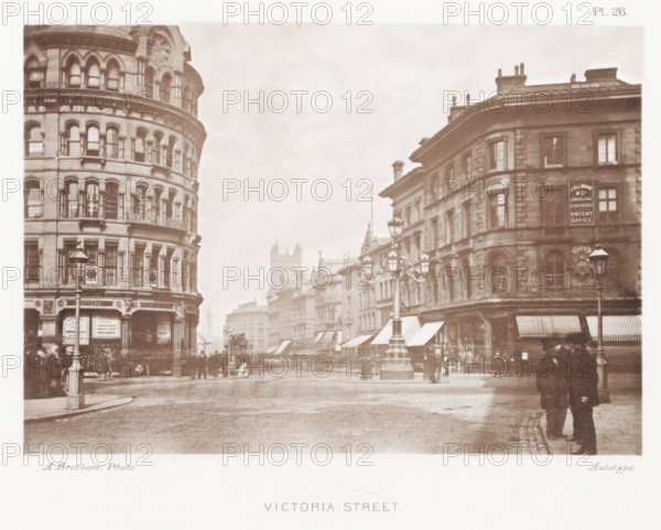 View of Victoria Street in Manchester, Victoria Street, page, photomechanical print, number: 'Pl. 26.', photographer: Brothers, Alfred, Manchester, cliché maker: anonymous, c. 1868 - in or before 1878, printer (person), paper, collotype, photoprint, height 131 mm x width 190 mm, Print after page 28., shop, store, street, A sepia-toned street scene showing multi-story stone buildings with rows of arched windows on either side of a broad cobbled road, a rounded corner building on the left and a rectangular corner building on the right, decorative street lamps with ornate posts standing in the middle and at the edges of the street, awnings over shopfronts along the ground floors, small groups of people standing and walking on the sidewalks, a horse-drawn vehicle and distant buildings fading into the haze down the street, and architectural details such as cornices, pilasters, and chimneys on the rooflines.