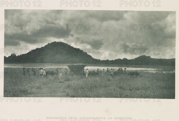 Tour group with bullock carts in Minneriya, Sri Lanka, page, photomechanical print, title: 'RETURNING FROM POLONNARUWA AT EVENTIDE.', photographer: Henry William Cave, Minneriya, cliché maker: anonymous, 1896, South Asia, paper, Woodburygravure, height 101 mm x width 196 mm, Print for page 103., 'en route', traveler under way, two-wheeled vehicle drawn by one animal, ox, A wide landscape photograph showing a grassy field in the foreground with a group of people standing and walking among two horse-drawn carts; one cart has a covered top and large wooden wheels while the other is more open and shows harnessed animals at the shafts; the people wear simple clothing and head coverings and some appear to be guiding the animals. Behind them is a strip of water reflecting the sky and a dark, tree-covered hill rising across the middle of the image. Above the hill a broad sky filled with heavy, textured clouds occupies the upper portion of the scene.