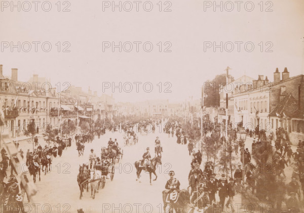 Bergerac- Voyage presidential- Place Gambetta, Le cortège, Place Gambetta, 2e vue, View of the entry of President Félix Faure on the Place Gambetta in Bergerac, photograph, page, Bergerac, 1895-06-04, photographer, paper, daylight gelatin silver print, height 118 mm x width 167 mm, square, circus, triumphal entry and public reception, pageant, 'entrée solennelle', 'joyeuse entrée', four-wheeled vehicle drawn by two animals, façade (of house or building), A wide street scene viewed from above with rows of multi-story buildings lining both sides and a large open road filled with people, horses, carriages, and riders moving toward the foreground; crowds stand on balconies and sidewalks along the buildings, some waving flags, while trees and tall poles with banners or lanterns line the street; many figures wear formal or uniformed attire and some riders wear plumed hats, with distant buildings visible down the avenue under a pale sky.