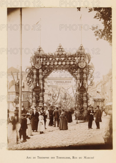 View of a triumphal arch in the Rue du Marché in Bergerac in honor of the entry of President Félix Faure, Arc de triomphe des tonneliers, Rue du Marché, photograph, page, Bergerac, 1895-06-04, photographer, paper, daylight gelatin silver print, height 161 mm x width 119 mm, street, triumphal arch, triumphal entry and public reception, pageant, 'entrée solennelle', 'joyeuse entrée', A street scene shows a large decorative archway made from stacked barrels, hoops, and foliage spanning the road, topped with round elements and flags on tall poles and flanked by ornate columns wrapped with garlands and rings; beneath the arch a banner is suspended and the street beyond is lined with buildings draped with more flags and hanging decorations. In the foreground a crowd of people wearing period clothing gathers on a cobbled street, including women in long dresses and hats, men in coats and hats, and children, with some people standing in groups and others walking. Two men in dark coats and hats ...