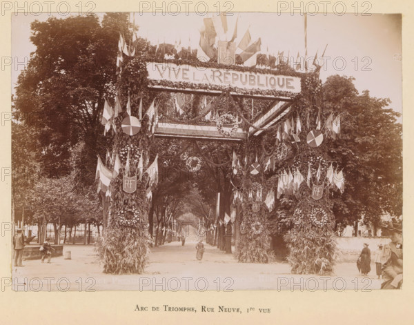 View of a triumphal arch on the Rue Neuve in Bergerac in honor of the arrival of President Félix Faure, Arc de triomphe, Rue Neuve, 1e vue, Bergerac- Voyage presidentialiel- Arc de triomphe, photograph, page, Bergerac, 1895-06-04, photographer, paper, daylight gelatin silver print, height 120 mm x width 169 mm, street, triumphal arch, triumphal entry and public reception, pageant, 'entrée solennelle', 'joyeuse entrée', A wide tree-lined avenue framed by tall leafy trees leads into the distance beneath a large decorated archway covered in foliage and floral arrangements, with numerous flags and garlands draped across the top and sides and circular floral wreaths and round emblems attached to the arch supports, while people in period clothing walk or stand along the avenue and at the base of the arch.