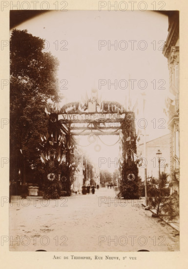 View of a triumphal arch on the Rue Neuve in Bergerac in honor of the entry of President Félix Faure, Arc de triomphe, Rue Neuve, 2e vue, photograph, page, Bergerac, 1895-06-04, photographer, paper, daylight gelatin silver print, height 167 mm x width 118 mm, street, triumphal arch, triumphal entry and public reception, pageant, 'entrée solennelle', 'joyeuse entrée', A sepia-toned street scene framed by tall leafy trees on one side and an ornate building facade on the other, with a decorated archway covered in foliage and garlands stretching across the road and topped with clustered flags and wreaths, flanked by vertical columns wrapped in foliage and additional hanging circular wreaths, small groups of people and blurred figures walking along the street beneath the arch, rows of buildings receding into the distance, a lamppost near the building, and a foreground of a wide bare roadway.