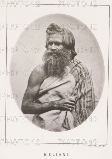 Beliani, page, photomechanical print, number: 'No. 26', photographer: Bourne & Shepherd, Nilgiris, photographer: Nicholas & Curths, cliché maker: anonymous, printer (person): Autotype Printing Company, London, c. 1863 - in or before 1873, printer (person), paper, collotype, photoprint, height 121 mm x width 99 mm, Print for page 215., adult man, A monochrome oval portrait of a bearded man shown from the torso up, with long hair pulled into a small top knot and a thick, full beard; he is draped in a plain cloth across his chest and a patterned textile over one shoulder, one arm folded across his body and the other arm partially visible, set against a light, softly shaded backdrop within a rectangular frame.
