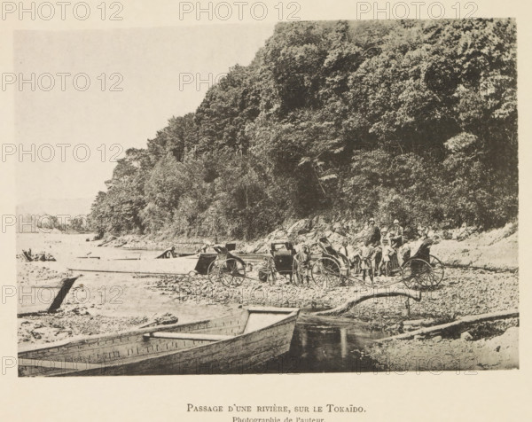 Passage d'une rivière, sur le Tokaïdo, Touring group with rickshaws on the bank of a river in Japan, page, photomechanical print, inscription: 'Photographie de l'autoriteit.', photographer: Hugues Krafft, Tokaido, cliché maker: anonymous, in or after 1882 - in or before 1883, Honshu, paper, collotype, photoprint, height 119 mm x width 172 mm, river, crossing a river, rickshaw, A sepia-toned scene shows a shoreline with a large wooded hillside occupying the right side and background, dense with trees and foliage. Several wooden rowboats rest in shallow water and on the shore in the foreground, their hulls visible and some partially beached. On the beach area near the base of the hill there are two-wheeled rickshaws with large spoked wheels and a group of people standing nearby, some wearing hats and simple clothing. The shoreline is scattered with rocks, logs, and debris, and the water surface appears calm. The overall image has a grainy, aged photographic quality.