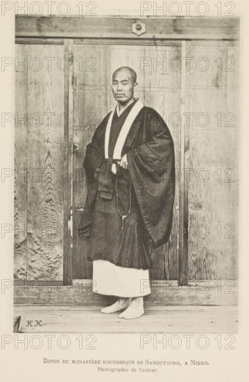 Buddhist monk in the Rinnoji temple in Nikko, Bonze du monastère bouddhique de Sambutsudo, a Nikko, page, photomechanical print, inscription: 'Photographie de l'autoriteit.', inscription: 'HK', photographer: Hugues Krafft, Rinnoji, cliché maker: anonymous, in or after 1882 - in or before 1883, Hugues Krafft, photographer, cliché maker, Kanto, Nikko, paper, collotype, photoprint, height 172 mm x width 122 mm, temple, shrine, Hinduism, Buddhism, Jainism, monk(s), friar(s), religious functions, A standing man with a shaved head wears layered dark robes with a contrasting light collar and a long beaded necklace draped from his hands, and he stands barefoot on a wooden floor in front of tall wooden panels with visible wood grain and a horizontal beam above, with a small decorative emblem centered on the beam.