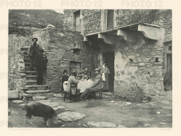 Breakfast company in Casta, Déjeuner à Casta, page, photomechanical print, photographer: Roland Napoleon Bonaparte, Corsica, cliché maker: Lemercier & Cie., Paris, c. 1881 - in or before 1890, paper, photoaquatint, height 118 mm x width 163 mm, Print on frontispiece., street, pig, breakfast - CC - out of doors, A worn stone courtyard in front of a rustic stone building with an arched doorway and a small balcony with a metal railing, a table covered with a cloth set for a meal with several seated figures wearing hats and coats, a standing woman in a headscarf near the doorway, rough stone steps up the left side with two standing figures on them, scattered stones and debris on the ground, and a pig grazing in the foreground.