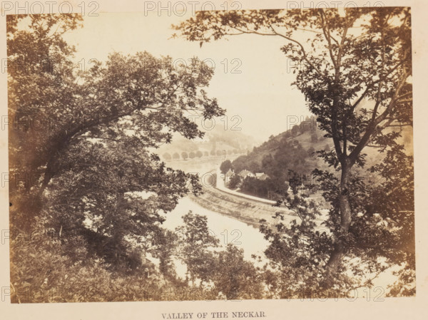 Valley of the Neckar, View of the River Neckar, photograph, page, photographer: Francis Frith, Germany, c. 1855 - in or before 1865, paper, albumen print, height 121 mm x width 169 mm, river, A sepia-toned landscape framed by tree branches and foliage in the foreground, with leafy canopies creating a natural border on left and right sides; a river curves through the middle distance, bordered by a winding road and railway track that follow the river's edge; a cluster of small buildings with pitched roofs sits near the riverbank beside the road, and hills rise behind them covered in trees and shrubs; distant hills and a line of trees along the far bank recede into a hazy background under a pale sky.