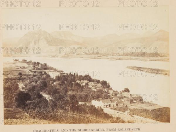 Drachenfels and the Siebengebirg, from Rolandseck, Siebengebirge with the Drachenfels seen from Rolandseck, photograph, page, photographer: Francis Frith, Remagen, c. 1855 - in or before 1865, Rhineland-Palatinate, paper, albumen print, height 116 mm x width 165 mm, mountain-top, peak, North Rhine-Westphalia, Königswinter, Drachenfels, A wide sepia-toned landscape showing a river with calm water running horizontally across the middle of the image, a cluster of houses with pitched roofs nestled among dense trees on the near bank, cultivated fields and orchards on the lower slopes in the foreground, a larger pale building set back among trees near the water, low rolling hills and rocky mountains rising on the far side of the river with terraced or striped slopes, scattered groves of trees along the opposite shore, and an open pale sky above.