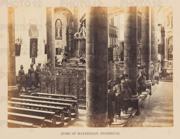 Grave monument for Emperor Maxilian in the Hofkerk in Innsbruck, Tomb of Maximillian, Innsbrück, photograph, page, photographer: Francis Frith, Hofkerk, c. 1855 - in or before 1865, Tirol, Innsbruck, paper, albumen print, height 123 mm x width 169 mm, grave, tomb, A sepia-toned interior view showing large stone columns in the foreground and background, ornate metalwork fencing with decorative patterns, rows of wooden benches, sculpted figures of armored knights standing on raised platforms, carved stairways and pedestals, framed paintings and arched wall niches, decorative architectural moldings and reliefs on the walls and ceilings, various sculptural elements and ornamental details arranged along the aisle and near the chancel area.