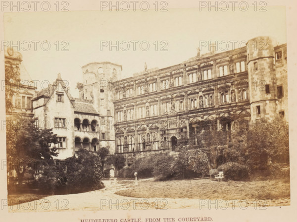 View of Schloss Heidelberg from the courtyard, Heidelberg Castle, from the Courtyard, photograph, page, photographer: Francis Frith, Heidelberg, c. 1855 - in or before 1865, Baden-Württemberg, paper, albumen print, albumendruk, height 122 mm x width 172 mm, courtyard, castle, Schloss Heidelberg, A sepia-toned photograph shows a large ornate stone building with multiple rows of windows and detailed sculptural decorations on its facade, adjoining a round tower with small rectangular openings and weathered stonework; to the left a smaller building with arched openings and a steep tiled roof connects to the larger structure, and a partial dome or roof element appears at the far left edge. In front of the buildings there is a garden area with trees and shrubs, a grassy lawn, a winding dirt path, and a pair of simple benches near the right side. The sky above is pale and empty, and the overall image has an aged, slightly faded appearance.