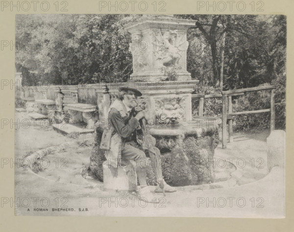 A Roman shepherd, page, photomechanical print, photographer: Samuel J. Beckett, Rome, c. 1890 - c. 1900, paper, collotype, photoprint, height 152 mm x width 202 mm, pipe, tobacco, old man, ornamental fountain, A sepia-toned scene shows a man sitting on a stone ledge beside an ornate stone fountain adorned with carved faces and decorative reliefs, the man wearing a hat and layered clothing with a cloth draped over one shoulder and holding a pipe to his mouth, a folded umbrella or walking stick rests by his knee and a worn bag lies near his feet, behind him a low balustrade with stone benches runs along a path and trees and foliage fill the background, a wooden railing stands to the right of the fountain.