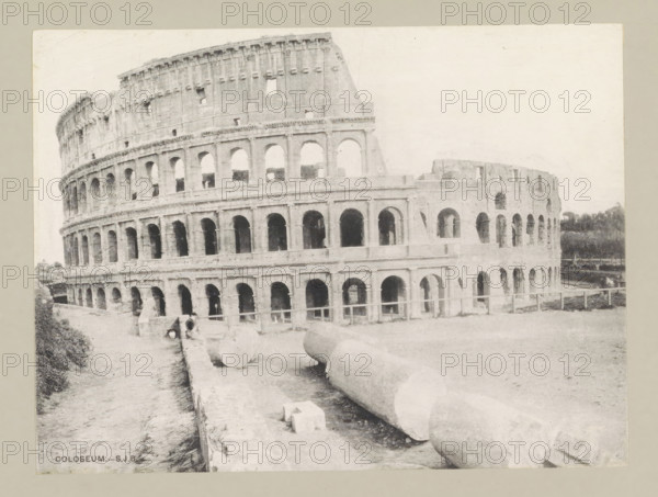 Coloseum, page, photomechanical print, photographer: Samuel J. Beckett, Rome, c. 1890 - c. 1900, paper, collotype, photoprint, height 151 mm x width 202 mm, facade (of house or building), theater (building), Colosseum, A wide photograph of a large stone amphitheater showing multiple tiers of rounded arches and rectangular openings, with worn and weathered masonry and broken sections along the upper edge; in the foreground there are large cylindrical stone fragments lying on the ground near a low wall, and a narrow path runs alongside the structure; sparse vegetation appears at the image edges and a low fence is visible near the base of the building.