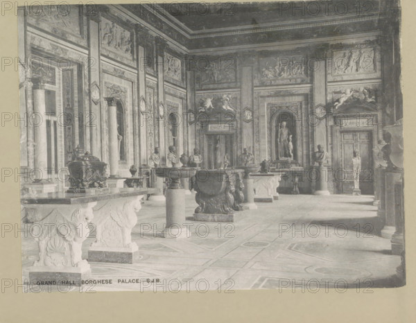 Grand hall Borghese palace, page, photomechanical print, photographer: Samuel J. Beckett, Palazzo Borghese, c. 1890 - c. 1900, Rome, paper, collotype, photoprint, height 152 mm x width 202 mm, vestibule, hall, hôtel, ie small palace in city, A wide interior view of an ornate classical hall with patterned stone flooring and tall decorative walls filled with framed reliefs and sculpted panels, fluted columns with carved capitals, and arched niches holding statues; several sculpted pedestals and ornate basins with decorative reliefs and lion-like supports occupy the central space, and busts on plinths line the room; the ceiling features layered moldings and decorative friezes, and the far wall shows a large statue in a recessed niche flanked by carved panels and a pair of doors with sculptural ornamentation.